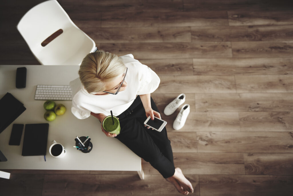 Tepuedoayudar: emprendedora haciendo una pausa en su actividad tomando una bebida , descalza apoyada en una mesa blanca,creando hábitos diarios de éxito, para su crecimiento personal, interno y empresarial.