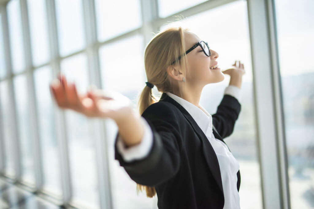 Tepuedoayudar: empresaria levantando los los brazos sonriendo y feliz por alcanzar su desarrollo personal y empresarial.